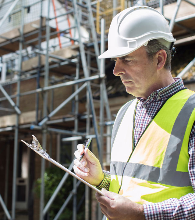 man-in-hard-hat-holding-clipboard-near-scaffolding-nebb-certification-for-firms