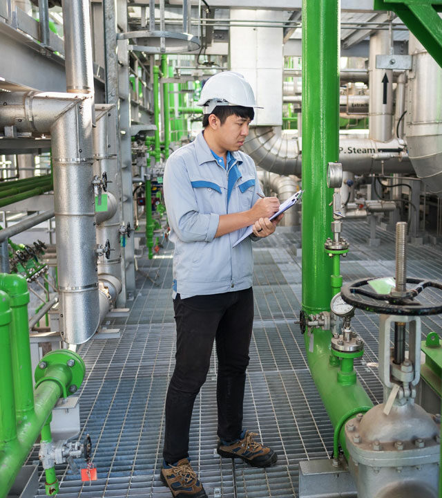 man-in-hard-hat-with-clipboard-standing-among-pipes-nebb-personal-certification